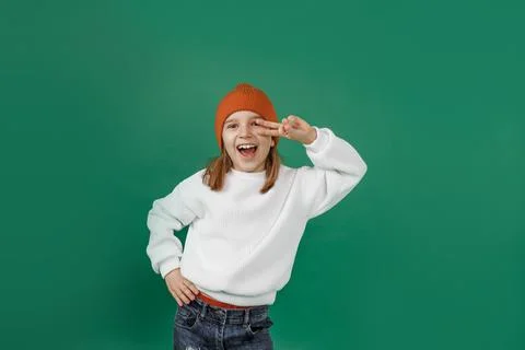 A boy in a white sweater and hat smiles and dances holding his fingers near h Stock Photos