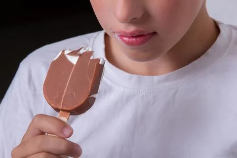 A boy whose face is unrecognizable eats ice cream covered in chocolate. Stock Photos