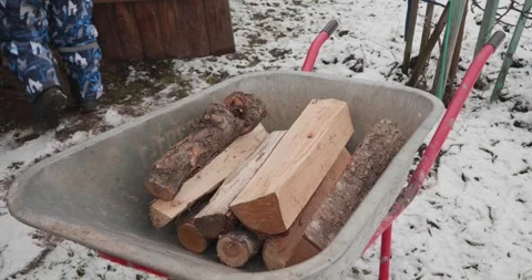 A boy in winter clothes carefully stacks firewood in a metal wheelbarrow on a Stock Footage 317240350
