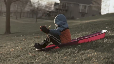 Boy in winter clothes on sledding hill wishes for snow Stock Footage