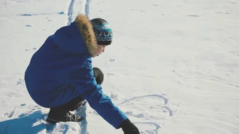 Boy In Winter Jacket and Hat Draws Hearts on the Snow with His Hand. Stock Footage 153325350