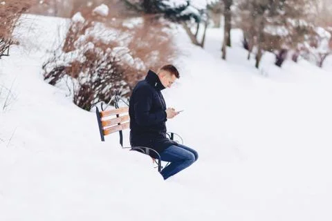 Boy in a winter jacket on a bench wrote sms Foto stock
