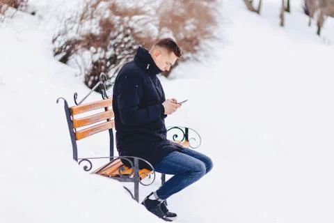 Boy in a winter jacket on a bench wrote sms Stock Photos