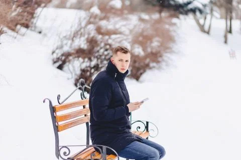 Boy in a winter jacket on a bench wrote sms Foto stock