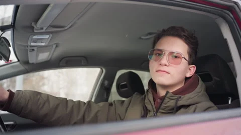 Boy in winter jacket rolling down car window with building reflection on glass Stock Footage 310180408