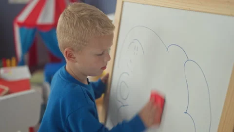Boy wiping whiteboard with red eraser, hand rubbing drawn cloud on board in.. Stock Footage 339256960