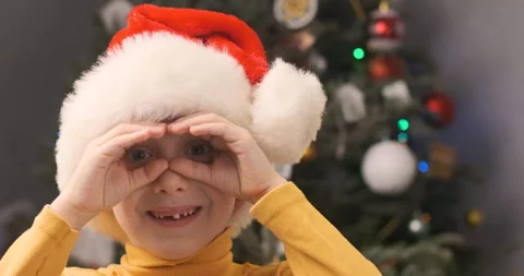 Boy without front teeth in Santa Claus hat, keeping hands like binocular Video stock 210467126