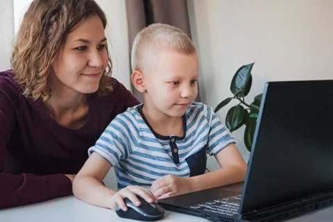 Boy working on a computer together with his mom at home. E-lessons, education Stock Photos