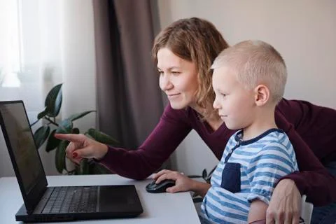 Boy working on a computer together with his mom at home. E-lessons, education Stock-Fotos