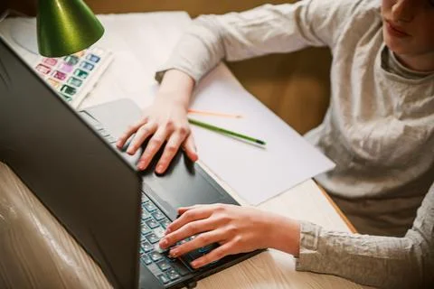 The boy writes down the task on a blank sheet lying near the laptop. Teenager Foto stock