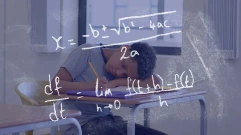 Boy writing at desk while lifting head, leading to chalkboard math formulas Stock Footage 334351994