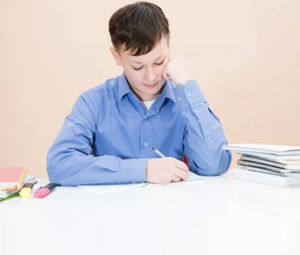The boy is writing in a notebook at the table Foto stock