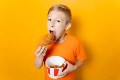 A boy on a yellow background eats fried chicken legs Stock Photos