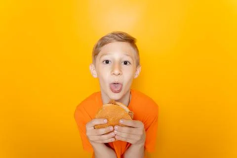 A boy on a yellow background eats a hamburger Stock Photos