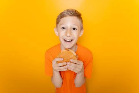 A boy on a yellow background eats a hamburger Stock-Fotos