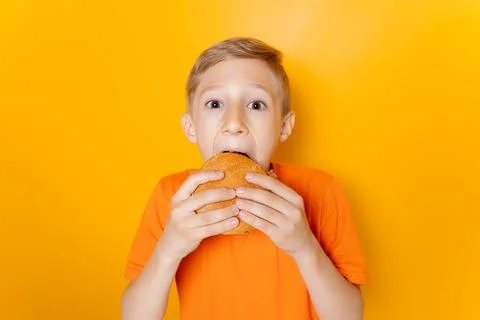 A boy on a yellow background eats a hamburger Stock Photos