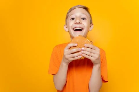 A boy on a yellow background eats a hamburger Stock Photos