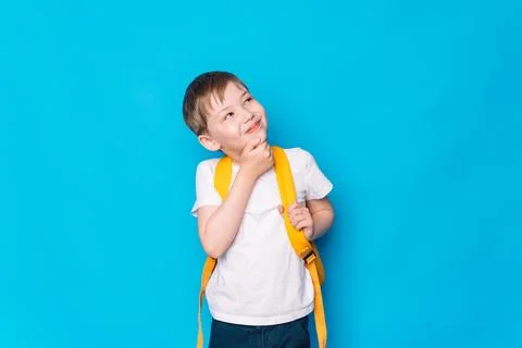Boy with a yellow backpack thought in front of a blue background Stock Photos
