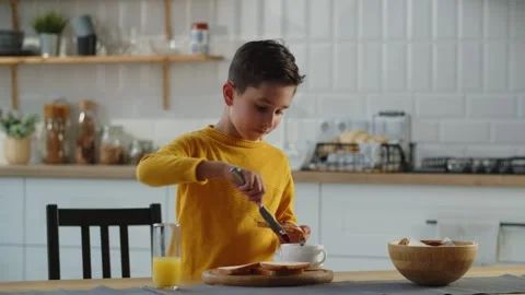 A boy in a yellow jacket holds a slice of bread in his hand and applies jam on Video stock 240195133