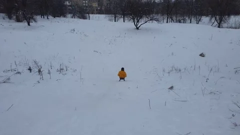 A boy in a yellow jacket is rolling down a hill on a sled. Winter activities Stock Footage 244527302