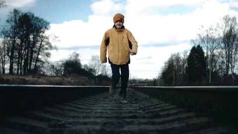 A boy in a yellow jacket runs along the rails towards the camera. He runs past. Stock Footage 194363566