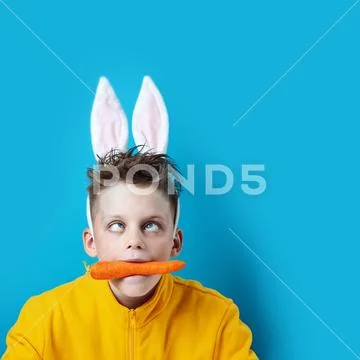 Boy in a yellow jacket with strabismus and hare ears, holding a carrot in his Stock Photos