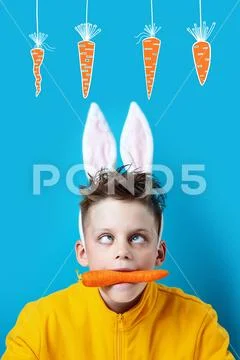 Boy in a yellow jacket with strabismus and hare ears, holding a carrot in his Stock Photos