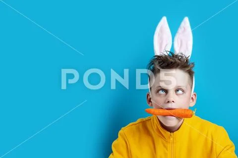 Boy in a yellow jacket with strabismus and hare ears, holding a carrot in his Stock Photos