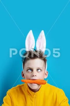 Boy in a yellow jacket with strabismus and hare ears, holding a carrot in his Stock Photos