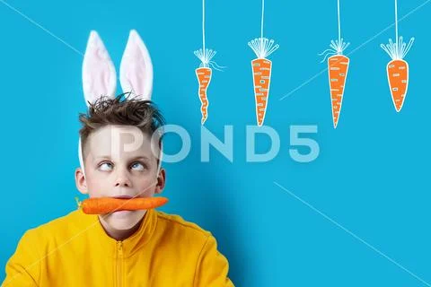 Boy in a yellow jacket with strabismus and hare ears, holding a carrot in his Stock Photos