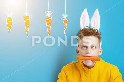 Boy in a yellow jacket with strabismus and hare ears, holding a carrot in his Stock Photos