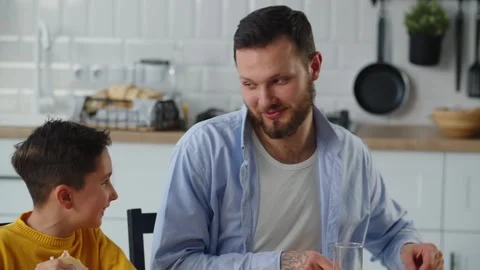 A boy in a yellow sweater sits in the kitchen with his father and eats Stock Footage 240725887
