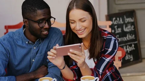 Boyfriend and girlfriend sitting at table in cafe and looking at smartphone Stock Footage 81834040