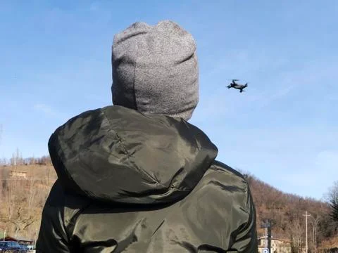 Boy's back in jacket playing with drone. And drone flying across blue skue   Stock Photos