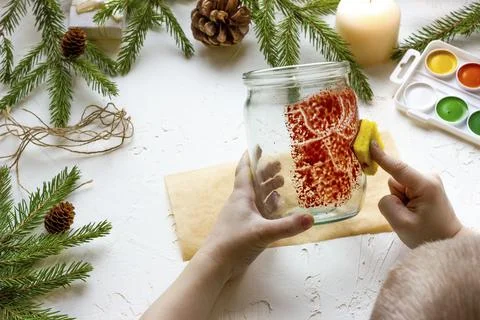 The boy's hands make a candlestick from a glass jar painted with red paint wi Stock Photos