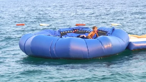 Boys jumping on trampoline, an inflated device at a water park. Stockbeeldmateriaal 80300628