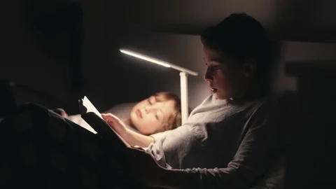 Boys lying in bed in dark and reading book. Stock Footage 171187330