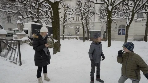 Boys play in Mirrabellgarten as snow falls and mom reads from phone Stock Footage 121753683