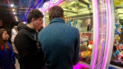 Boys playing a amusement machine with a hook that catches stuffed animals, 4k Stock Footage 198892499