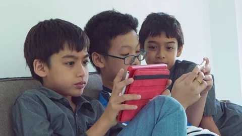Boys sitting on sofa and playing games on mobile phone Stock Footage 105631079