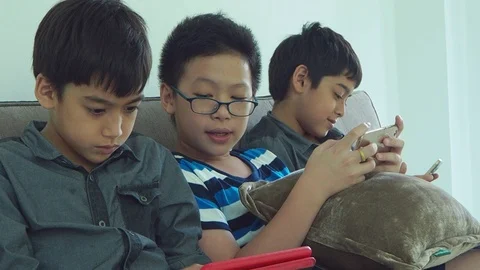 Boys sitting on sofa and playing games on mobile phone Stock Footage 105631292