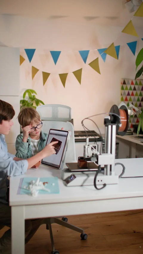 Boys study a drawing of a part on a tablet, currently printing on a 3D printer Stock Footage 335394859