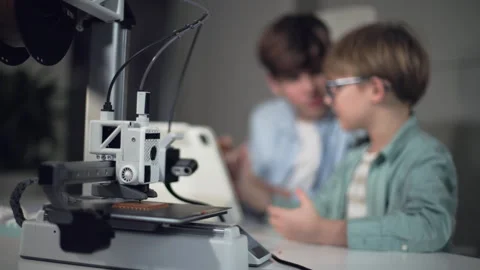 The boys at a table with a working 3D printer, observing and operating it Stock Footage 335378123