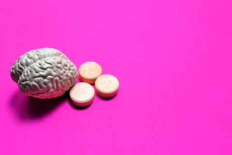 Brain model beside orange tablets on pink background symbolizing cognitive .. Fotos de archivo