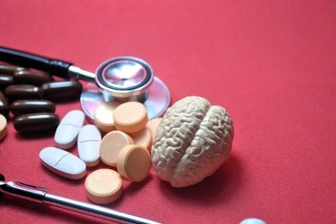 Brain model with stethoscope and assorted pills on red surface highlighting.. Stock Photos