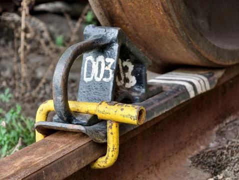 Brake chock securing a rusty metal train wheel on a rusty railway rail prev.. Stock Photos