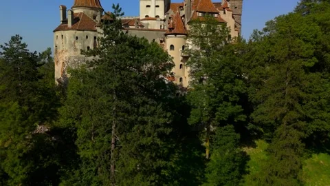 Bran Castle emerging above dense green forest and revealing the surrounding vill Stock-Footage 324840107