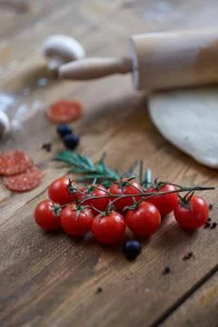 Branch of cherry tomatoes lying on table. Different ingredients unfocused Stock Photos