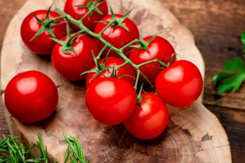 Branch of fresh cherry tomatoes with greens on a brown wooden background. Stock Photos