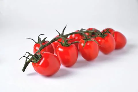 A branch of red cherry tomatoes sharp in front and blurred from behind on a w Foto stock
